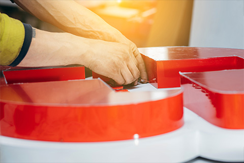 person assembling a large red number 14 sign in a workshop with visible hands carefully fitting the pieces together
